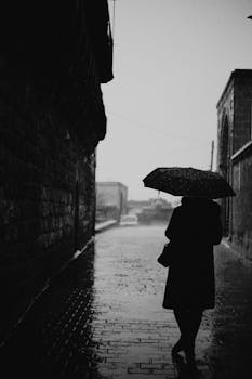 Black and white photo of a woman with umbrella on a rainy street in Mardin, Turkey.