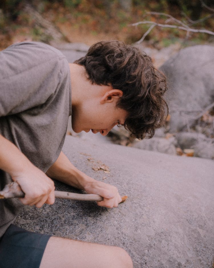 Man With Stick Near Stone In Forest