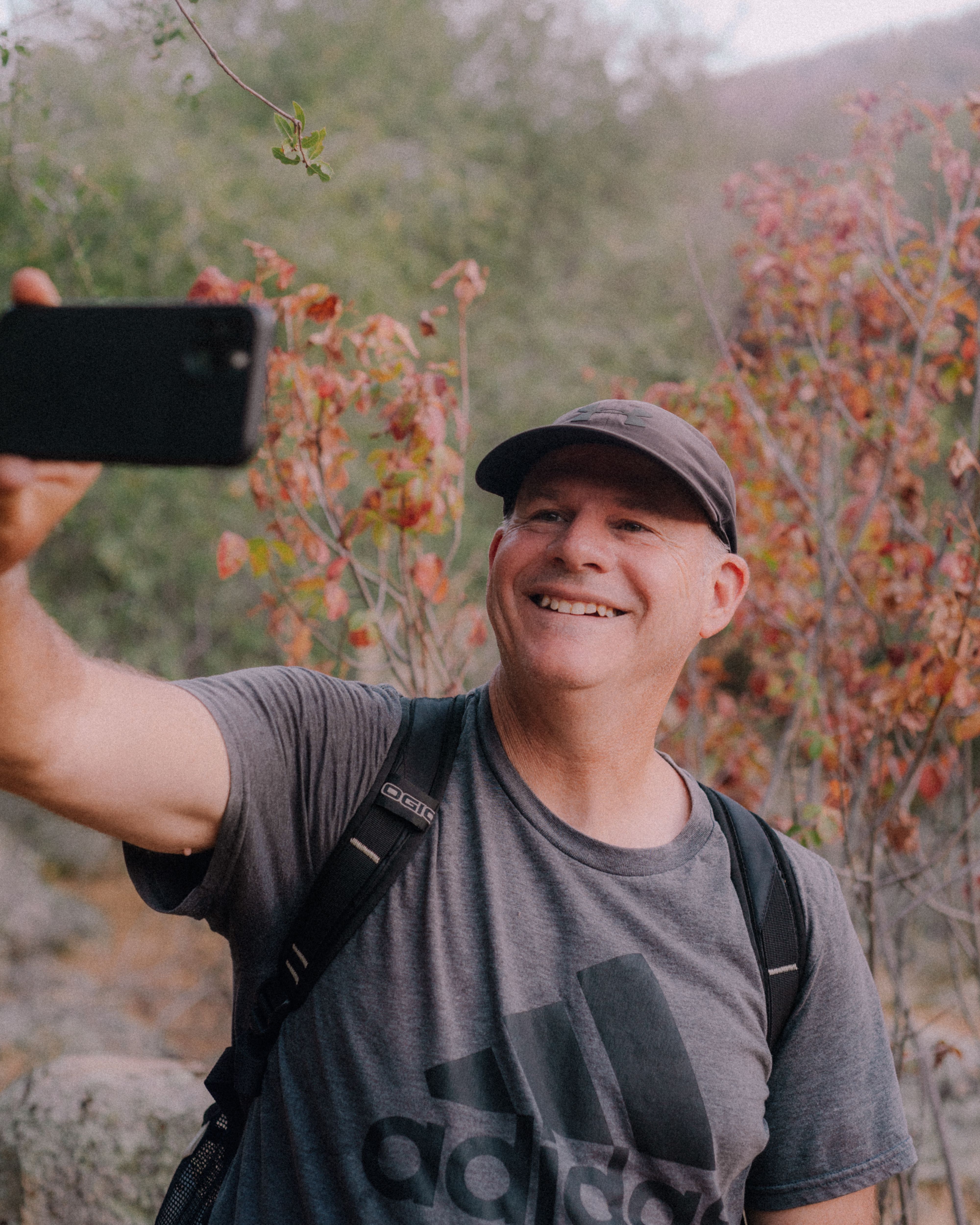 A smiling man takes a selfie while hiking outdoors, capturing the joy of adventure.