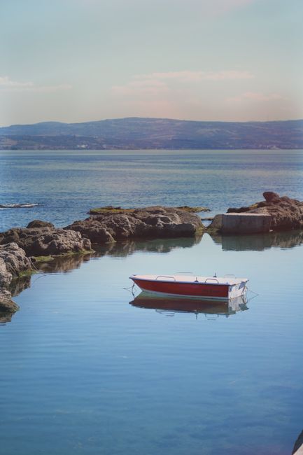 A peaceful red boat resting on calm ocean waters, surrounded by rocky landscape.