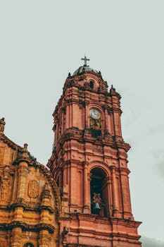 Elegant pink stone clock tower in Tlalpujahua de Rayón, capturing historic architecture with moody sky.