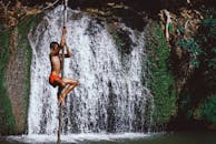 在泰国一处风景优美的瀑布旁，一个小男孩白天爬树