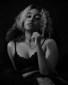 Monochrome portrait of a woman posing in lace lingerie with curly hair and necklace.
