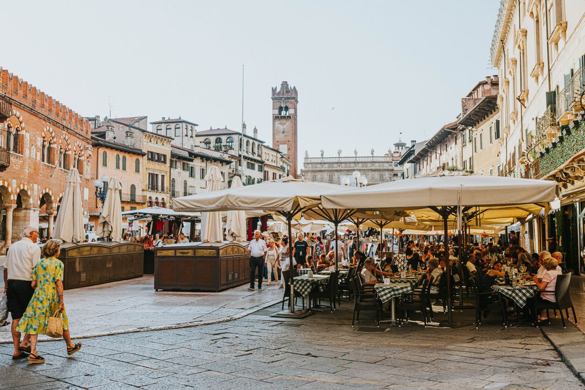 Piață dintr-un oraș italian cu terase pline de turiști sub umbrele mari