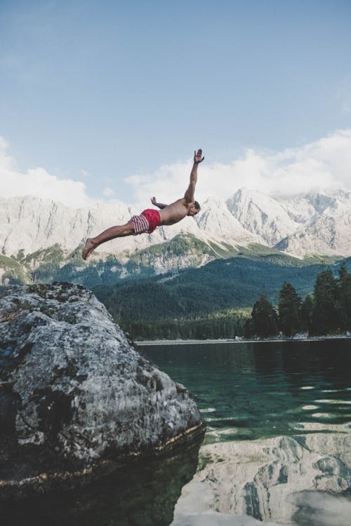 Free Man Wearing White and Red Board Short Diving from Rock Formation Stock Photo