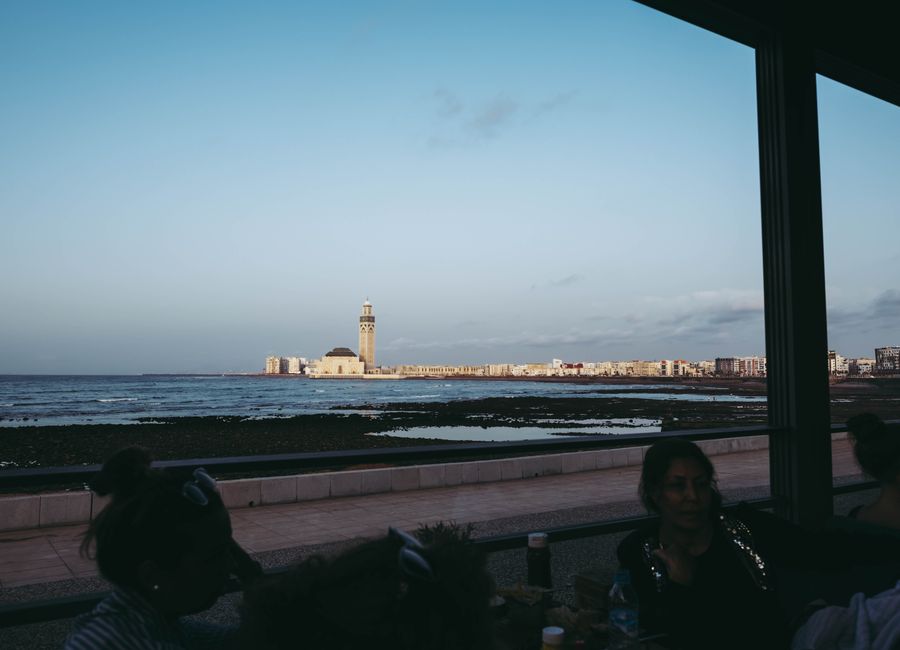 Scenic view of Hassan II Mosque from the Casablanca coastline during daytime with people in a café foreground.