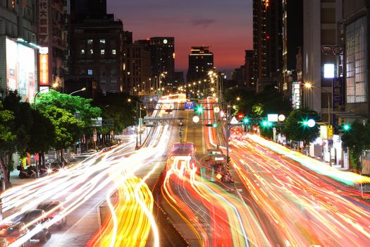 Long exposure of Taipei's urban traffic at dusk, showcasing colorful car lights and modern architecture.