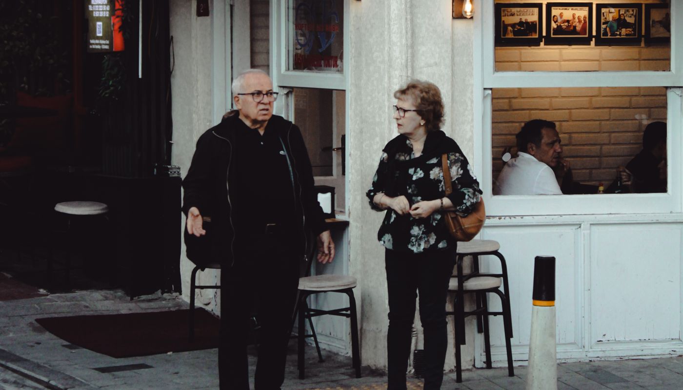 Two people standing outside a small café in the evening, mid-conversation on the pavement