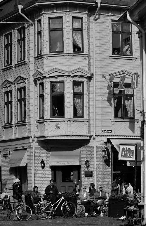 Free Black and white image of an urban street scene with people sitting outdoors in front of a historic building. Stock Photo