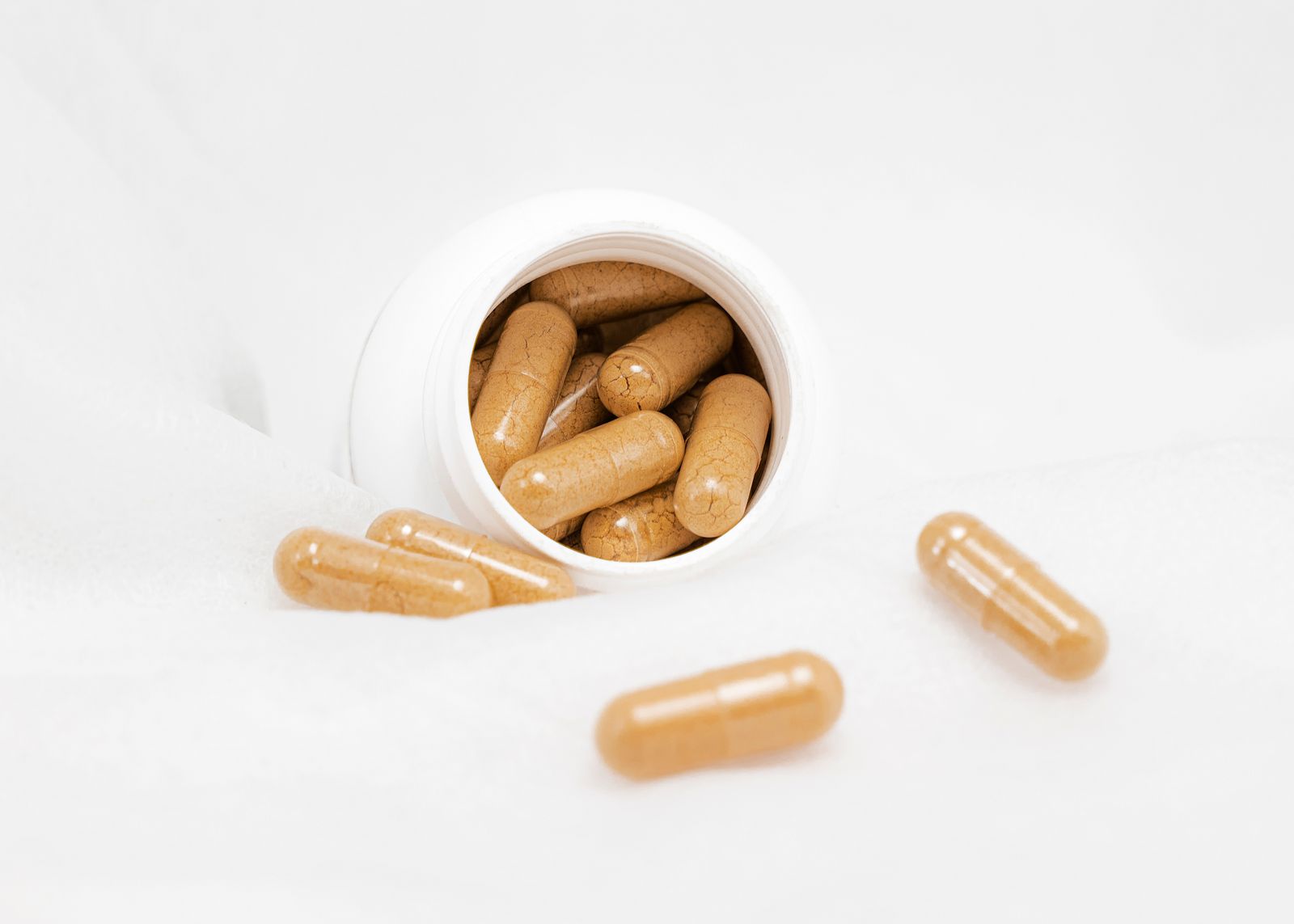 A shelf's worth of generic supplement capsules spilling from an unlabeled bottle
