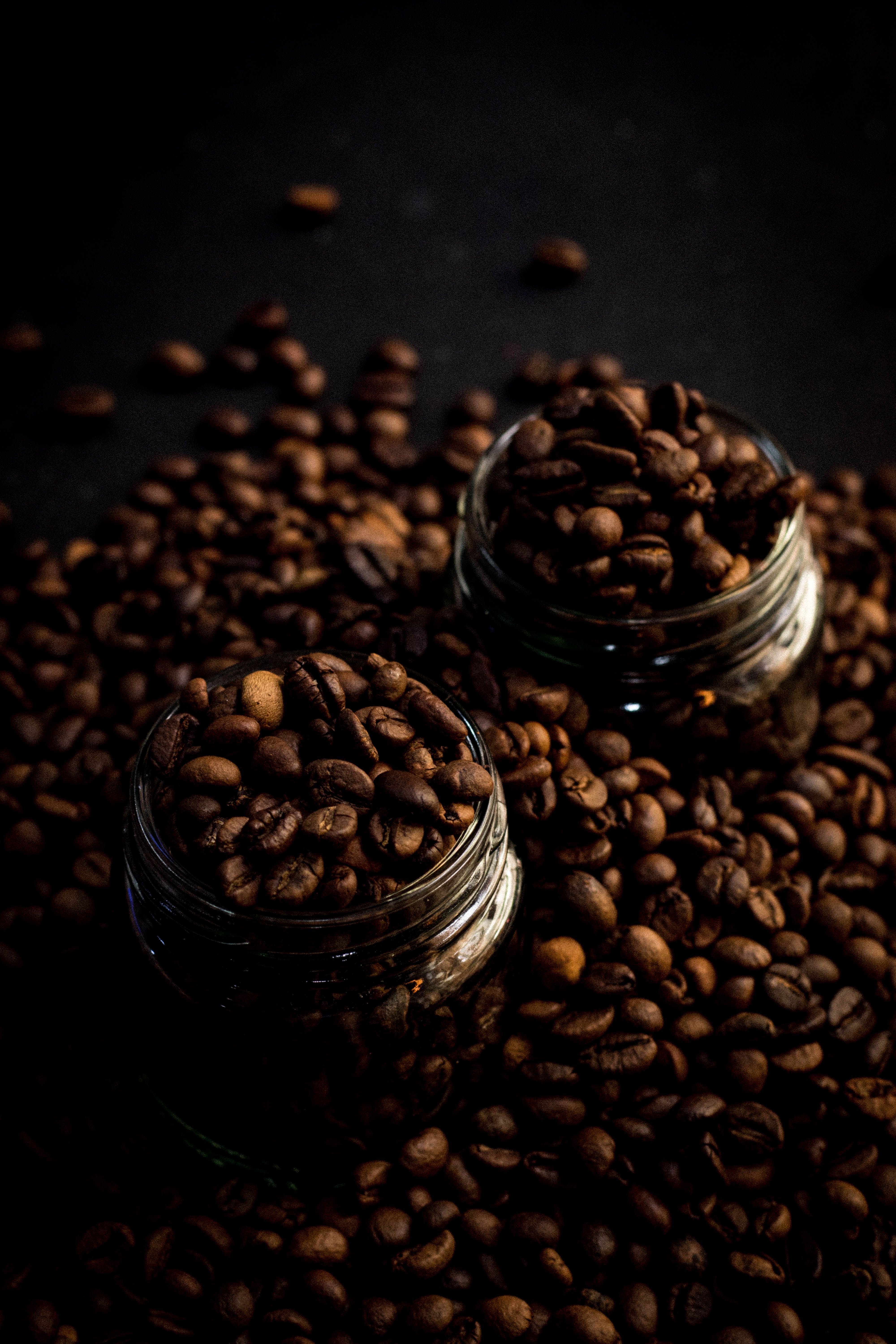 two glass jars overflowing with dark roasted coffee beans on a black background.