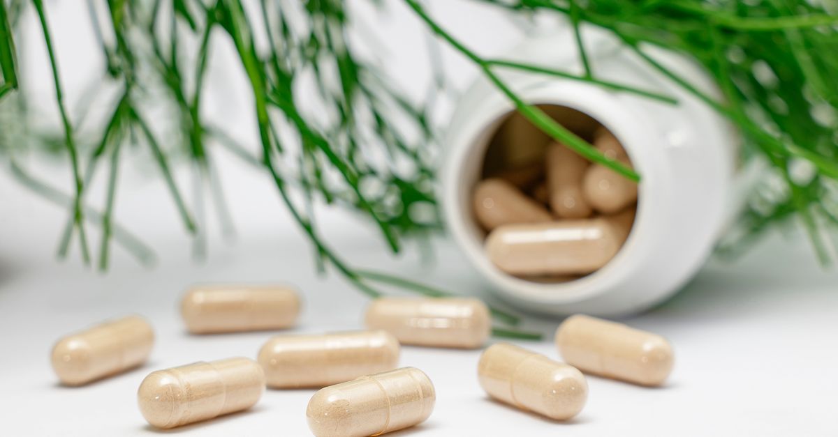 Close-up of herbal capsules spilling from a bottle with green plants in the background. - Evidence evidence guide for lactoferrin supplementation immune randomized trial