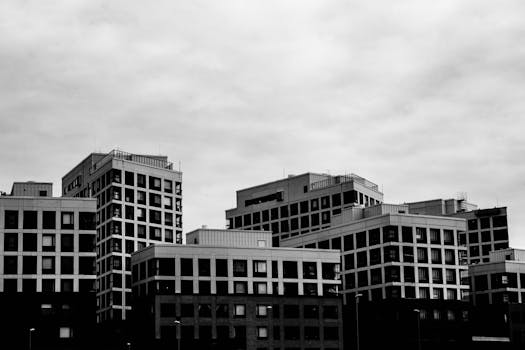Black and white cityscape featuring modern high-rise buildings under a cloudy sky.