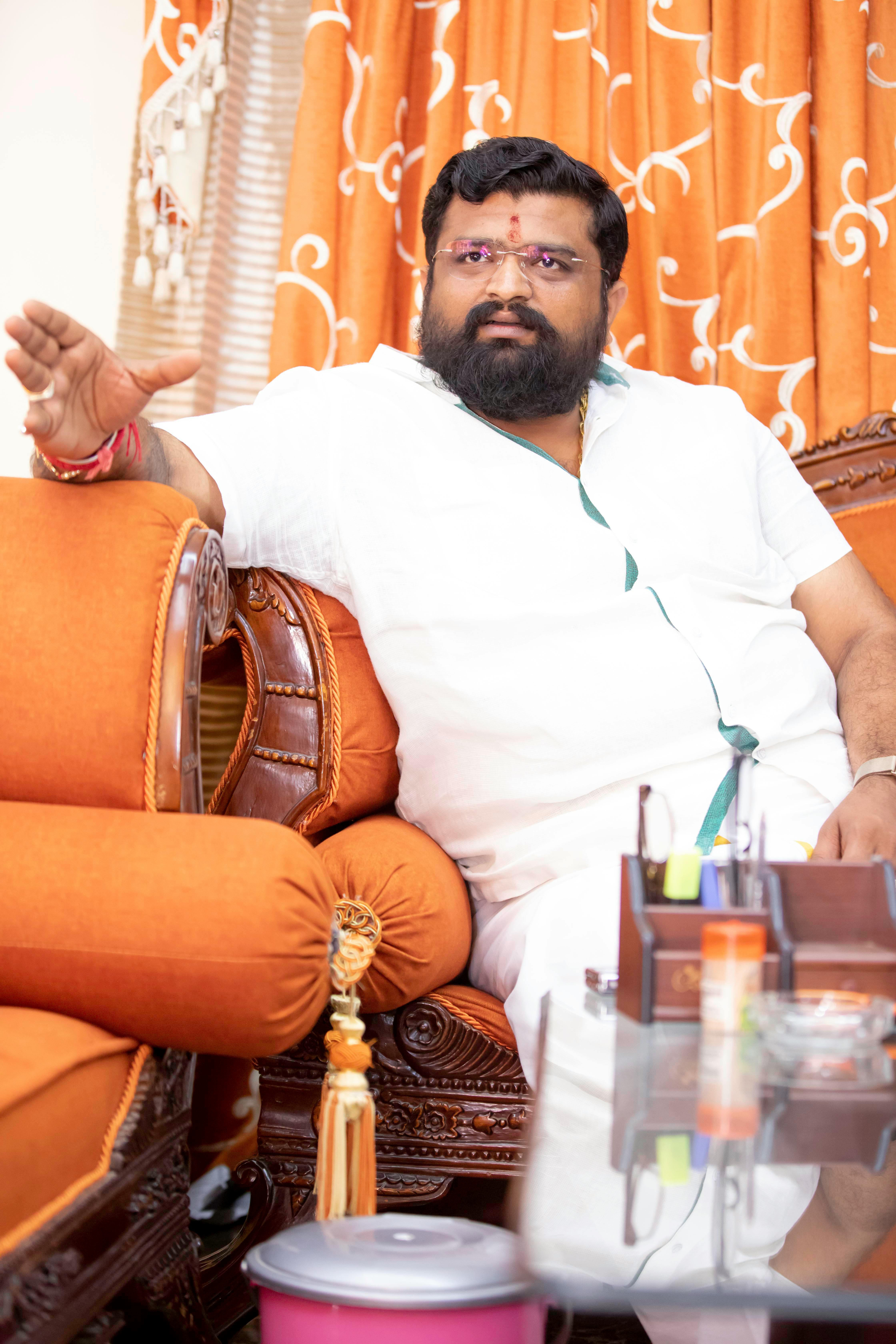 Asian man in traditional attire relaxing indoors on a couch with ornate decor.