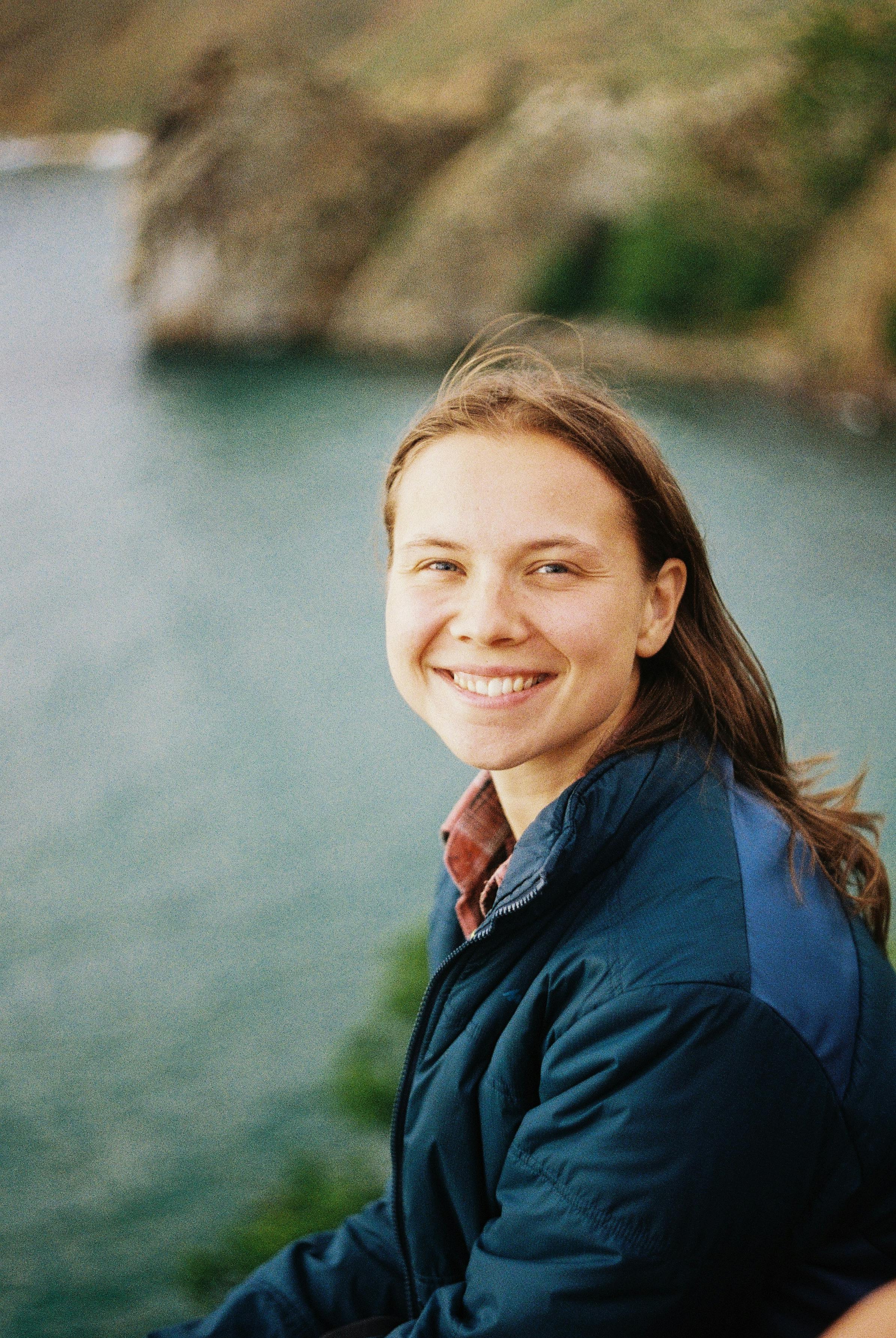 Caucasian woman with brown hair smiling near a scenic coastal view.