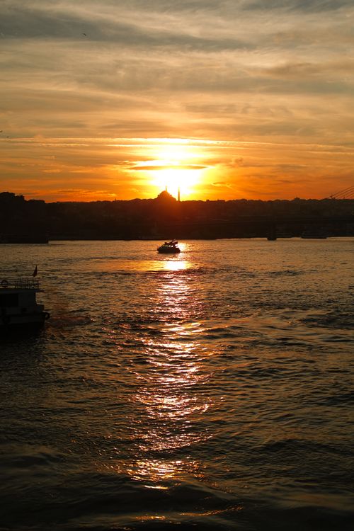 Free A peaceful sunset with a boat reflecting on the calm city waters, creating a golden serene scene. Stock Photo