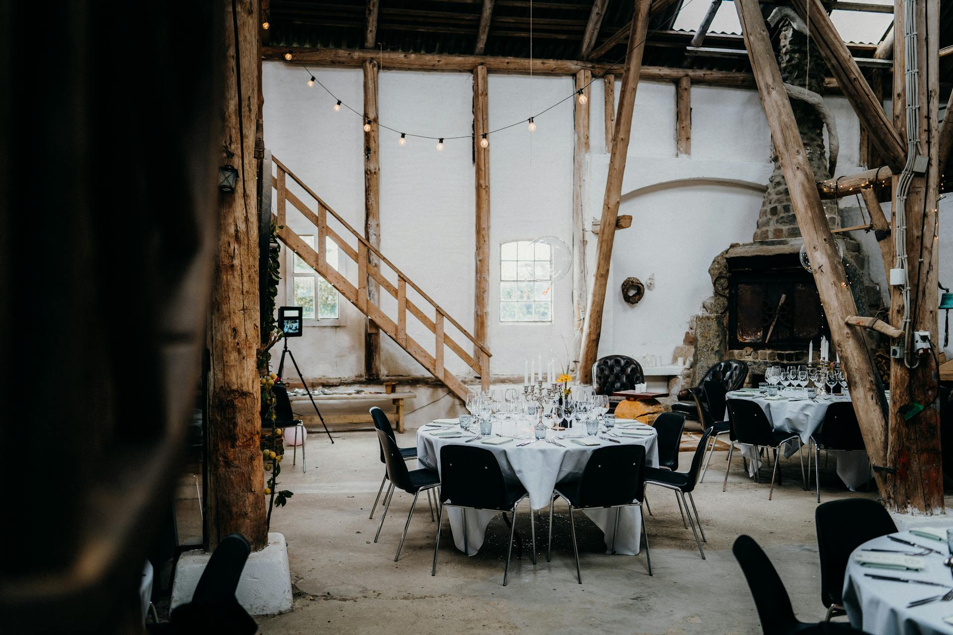 Charming rustic wedding reception setup in a barn with round tables and minimalistic decor.