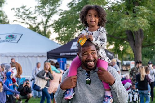 Free A joyful father carrying his daughter at an outdoor festival surrounded by people and tents. Stock Photo