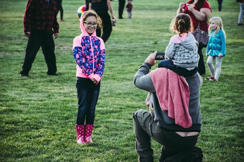 Man Carrying Toddler on His Neck Taking Photo of Standing Girl in Front of Him