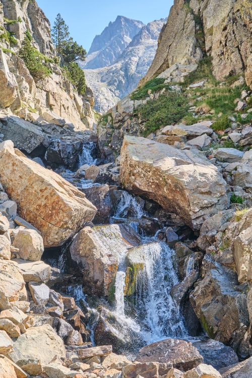 Free A tranquil mountain waterfall cascading over rocks under a clear blue sky. Stock Photo