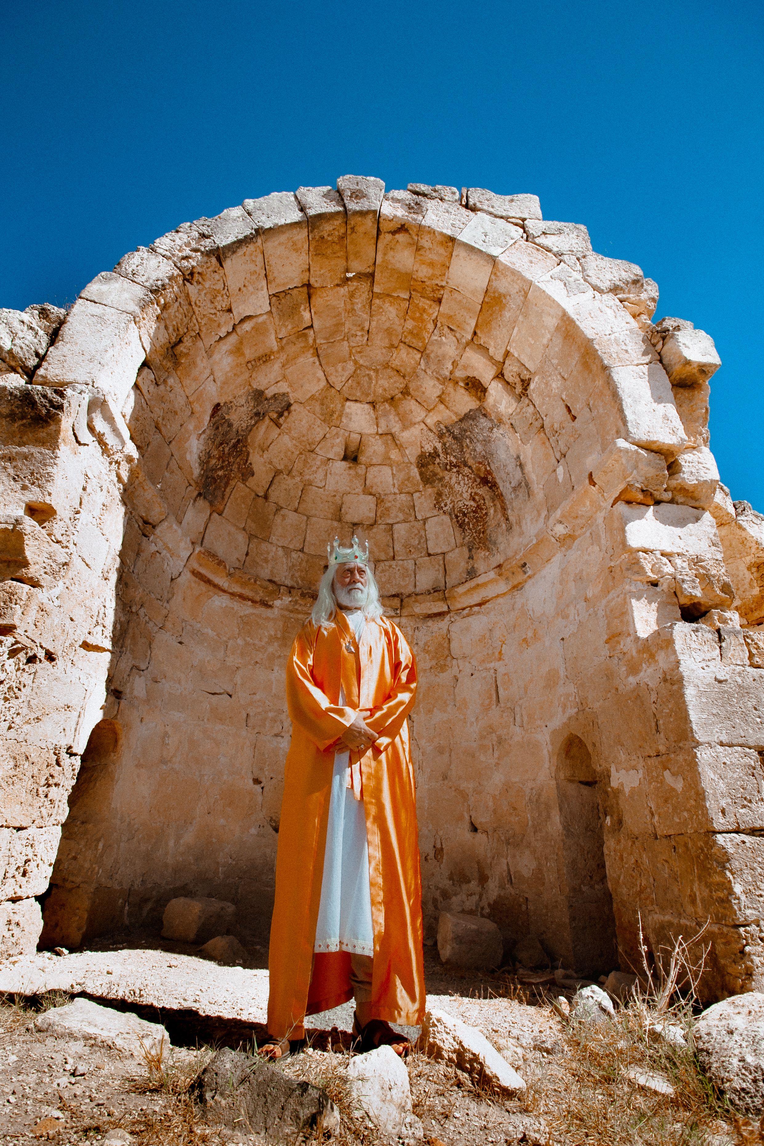 Elderly man in king costume stands in ancient ruins in Adana, Turkey.