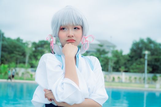 Woman in cosplay with white hair, posing thoughtfully near a pool.