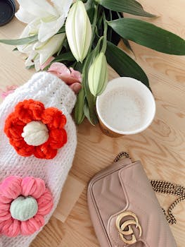 A cozy scene with coffee, a bouquet, and knitted sweater on a wooden table.