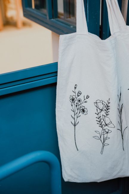 Stylish eco-friendly tote bag with floral embroidery hanging on a blue door. - The Impact of Climate on Handbag Care in Pakistan