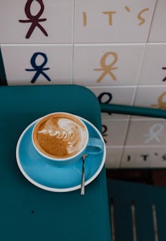 Cappuccino with latte art in a blue cup on a teal table, showcasing modern café vibes.