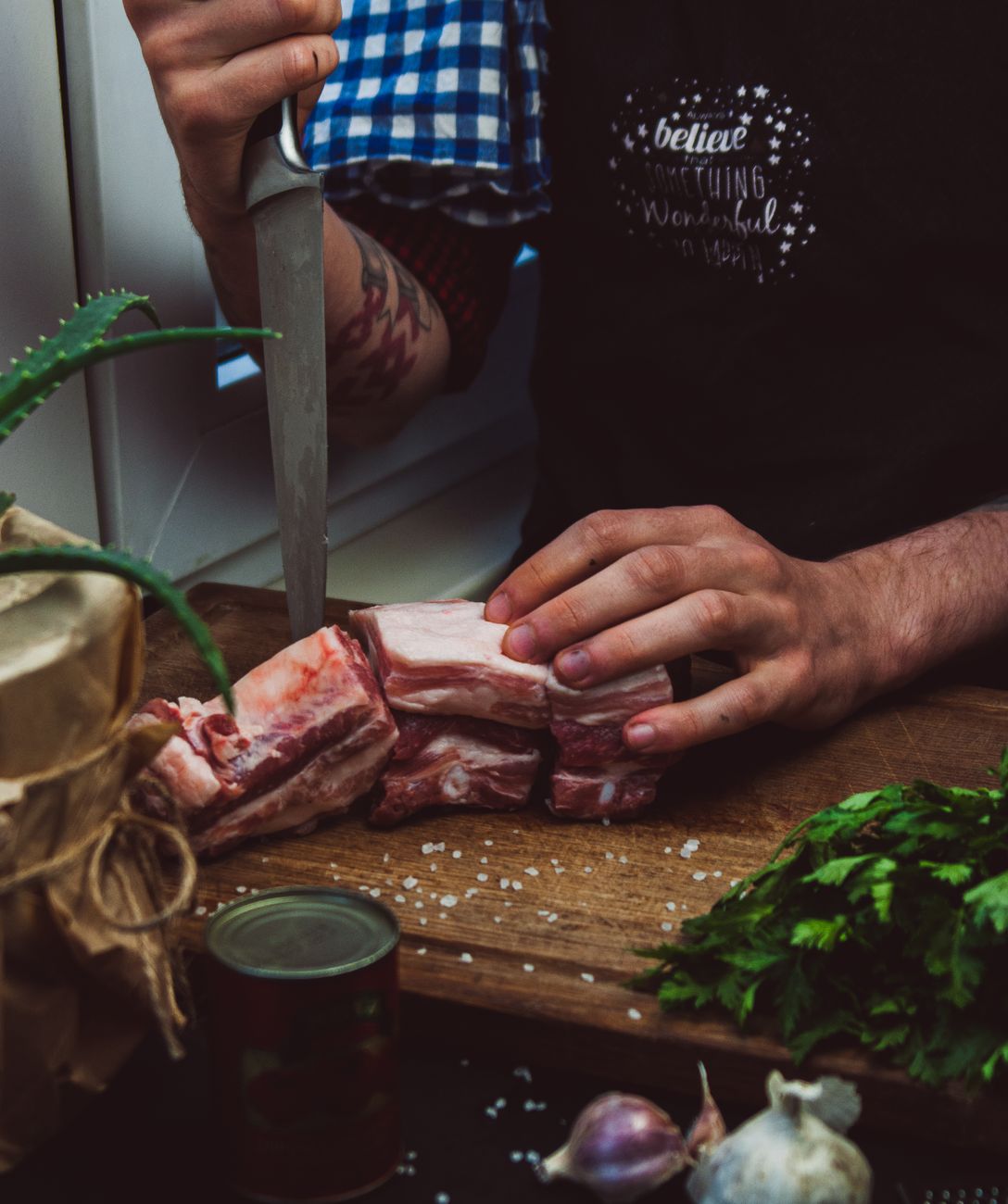 A butcher expertly slices raw meat with fresh herbs on a wooden table