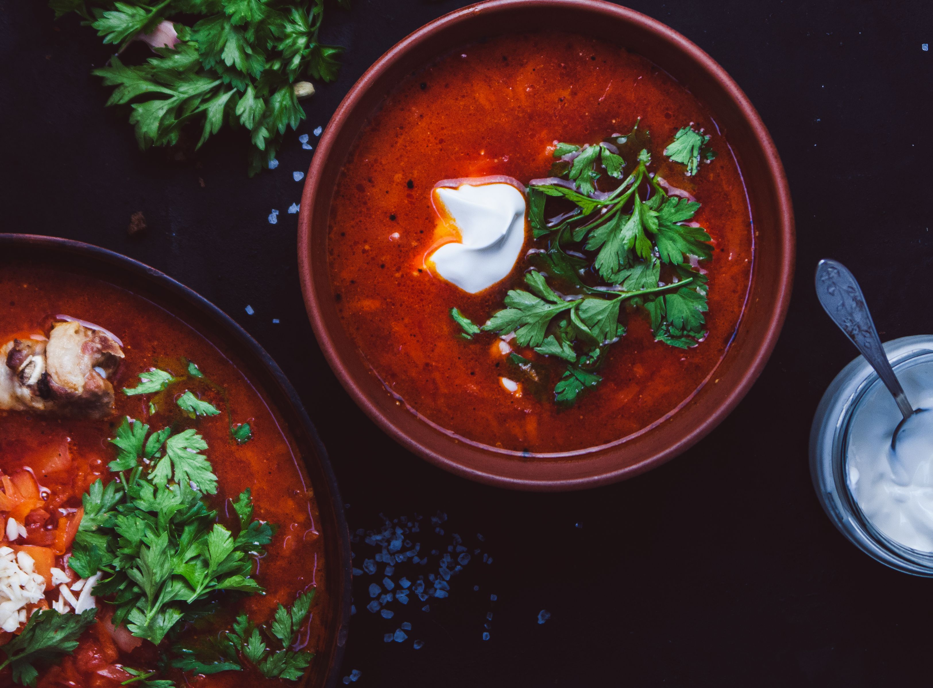 Top-down view of rich tomato soup garnished with fresh herbs and cream.