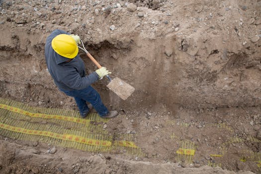 Overhead view of a construction worker digging a trench using a shovel at a site.
