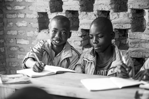 Free Black and white photo of two children studying with notebooks and pens against a brick wall. Stock Photo