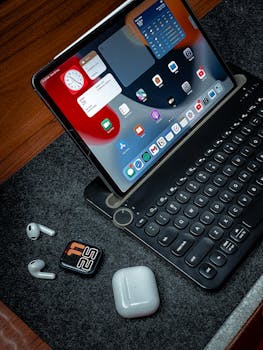 Digital workspace featuring a tablet, wireless earbuds, and a digital watch on a wooden desk.