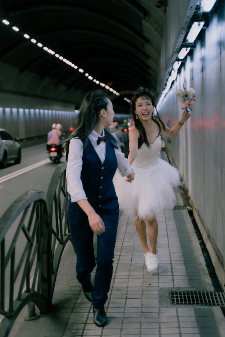 Bride And Bridegroom Running On Sidewalk In Tunnel