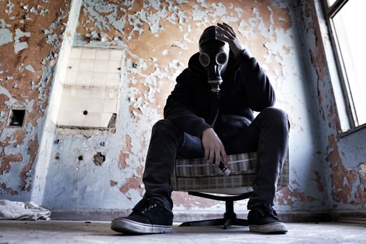 A man wearing a gas mask is seated in a dilapidated room, conveying a sense of despair and survival.