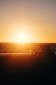 Stunning beach sunset with a silhouette of a lifeguard post and calm ocean waves.