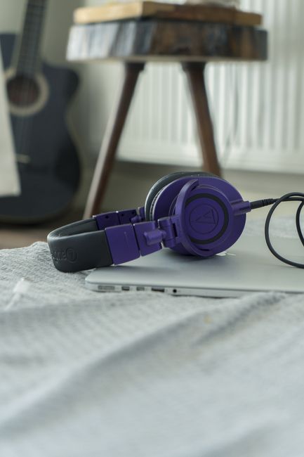Purple headphones rest on a laptop with an acoustic guitar in the backdrop, capturing a casual music vibe.
