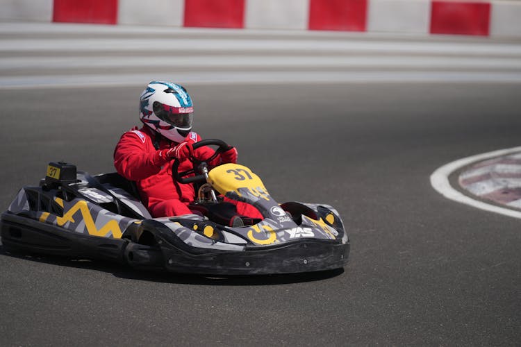 A Man In Red Racing Uniform Riding A Race Kart