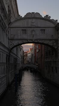 Dramatic view of a historic bridge over a Venetian canal at dusk, reflecting architectural charm.