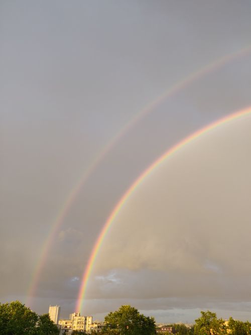 Free A striking double rainbow arcs over a city skyline against a dramatic cloudy sky. Stock Photo