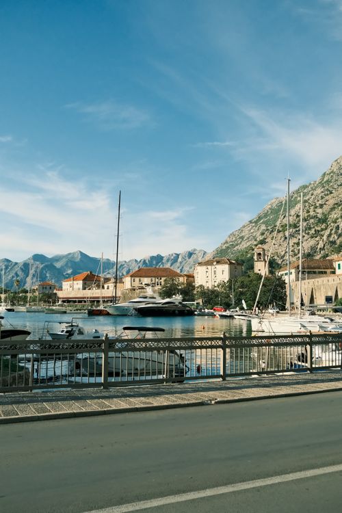 Free Coastal town marina with yachts and mountains under a clear blue sky, offering a serene urban escape. Stock Photo