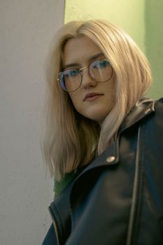 Portrait of a young Caucasian woman with blonde hair wearing a leather jacket and glasses.