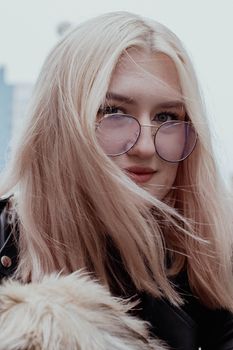 Close-up of a stylish woman with blonde hair wearing trendy eyeglasses outdoors.