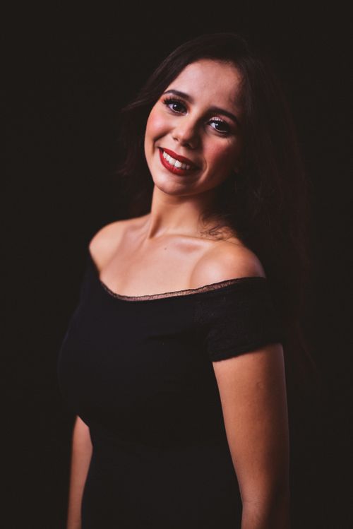 Free Smiling woman in an off-shoulder black dress posing against a dark background. Stock Photo