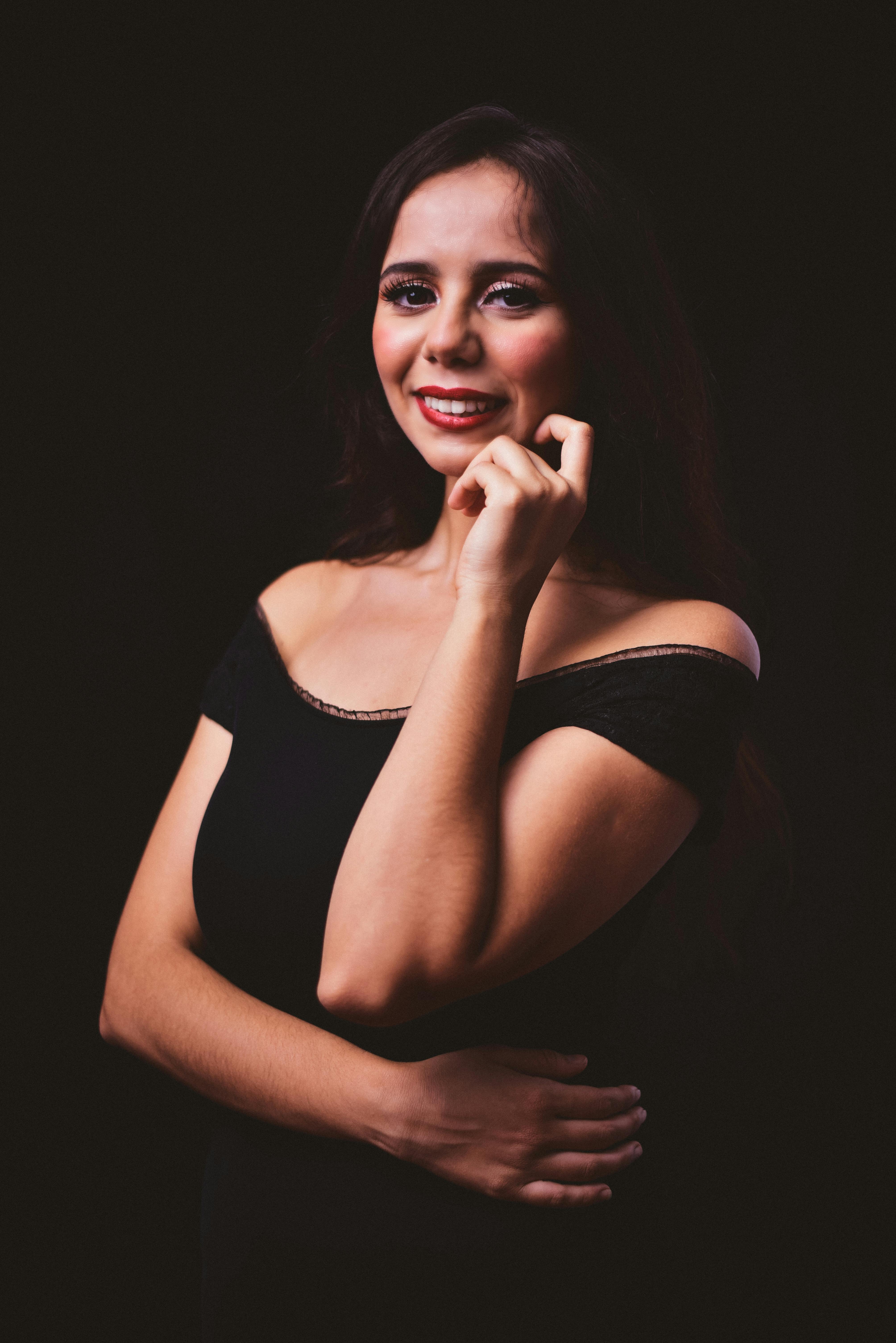 A stunning studio portrait of a smiling woman in an elegant black dress with red lips.