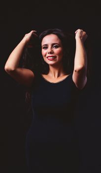 Portrait of a smiling woman in a black dress with a dark background, exuding elegance.