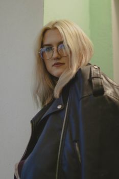 Blonde woman with eyeglasses wearing a black leather jacket indoors.