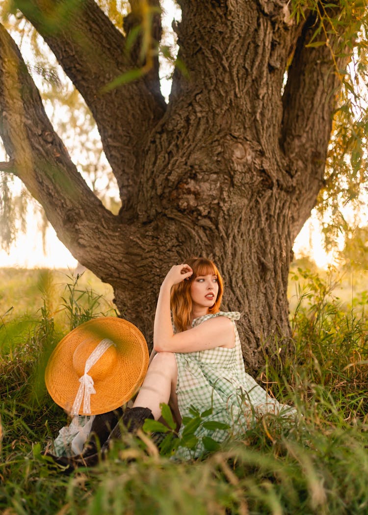 Beautiful Woman With A Hat Sitting Under A Tree In The Setting Sun 