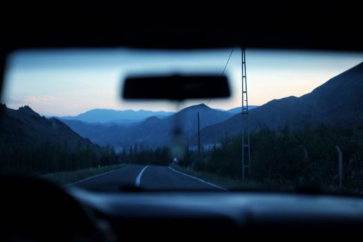 Capturing the serene view through a car windshield on a winding mountain road at twilight.
